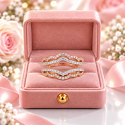 Two rose gold rings with pavé-set clear stones are displayed in an open pink velvet ring box, surrounded by soft pink roses and white baby's breath flowers.