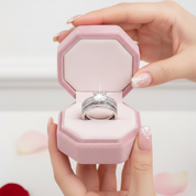 Pink jewelry box with a ring inside, held by a hand on a light background