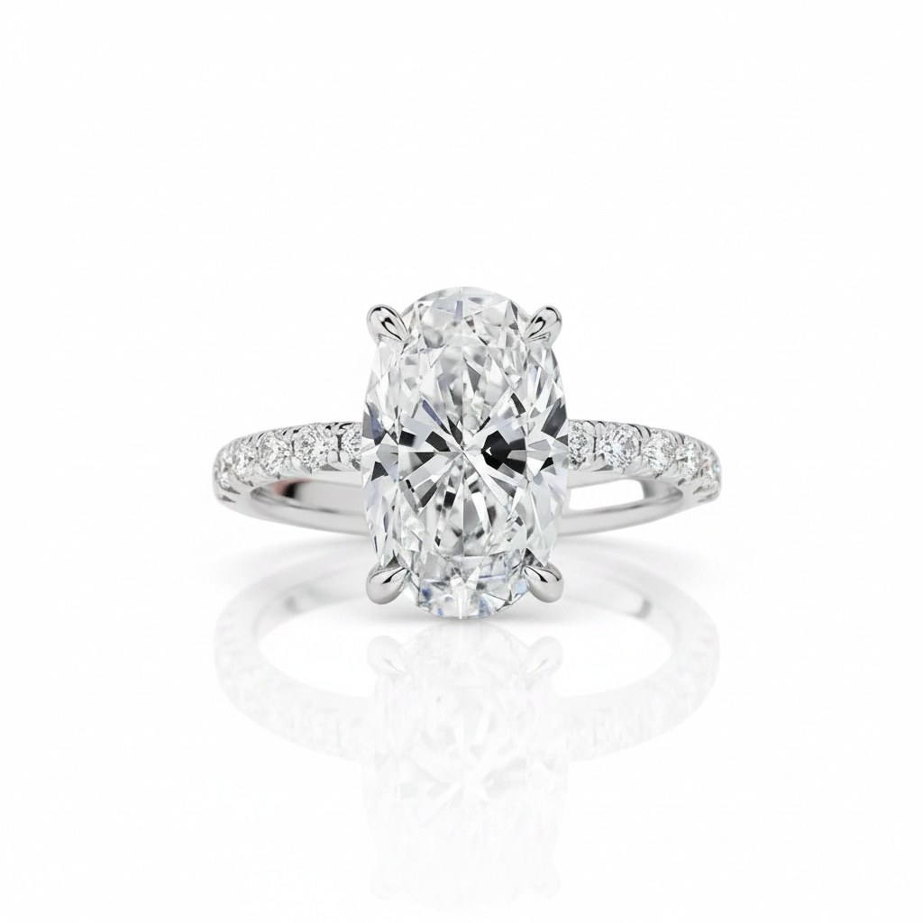 An oval diamond engagement ring with a radiant cut center stone in a six-prong setting, featuring a pavé diamond band, shown on a clean white background with a soft reflection below.