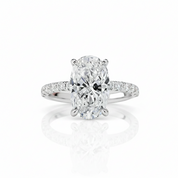 An oval diamond engagement ring with a radiant cut center stone in a six-prong setting, featuring a pavé diamond band, shown on a clean white background with a soft reflection below.