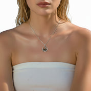 A close-up of a woman wearing a delicate silver necklace with a circular pendant featuring a small black bird, paired with a white strapless top.