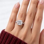 A close-up of a hand wearing a radiant-cut diamond engagement ring in a silver-toned band, with a burgundy knit sleeve visible at the wrist.