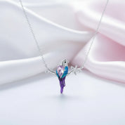 A silver necklace with a bird-shaped pendant featuring purple, blue, and pink crystal details, displayed on a soft white and pink satin background.