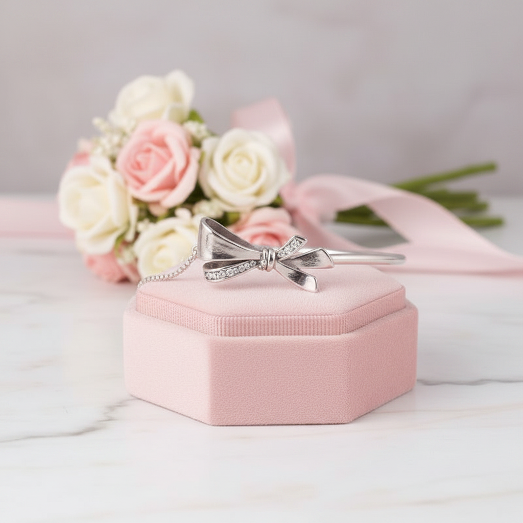 Silver bow-shaped ring on a pink jewelry box with flowers in the background