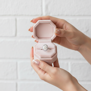 Hand holding a pink jewelry box with a diamond ring on a light background