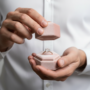 Person holding a pink jewelry box with an engagement ring inside, wearing a white shirt.