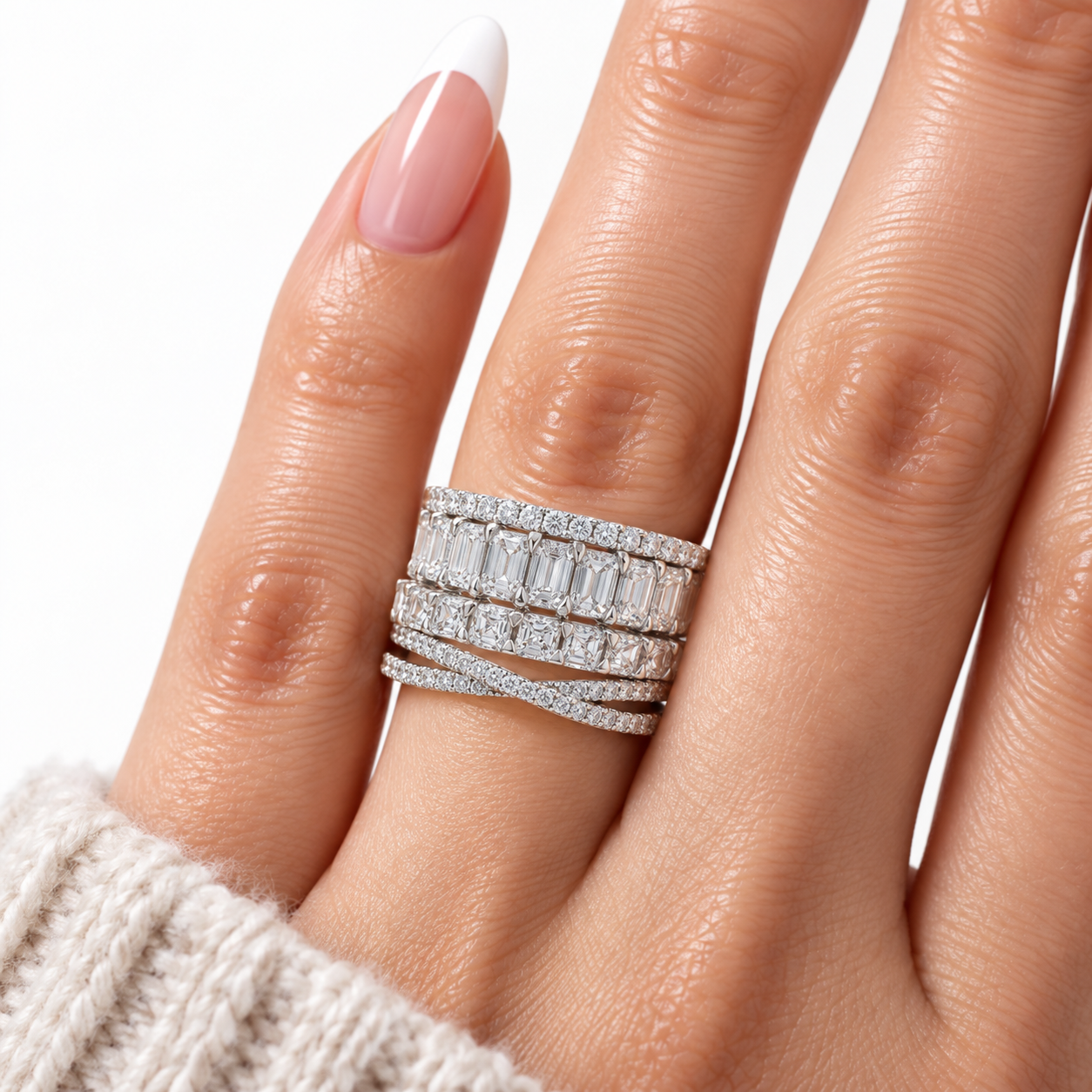 A close-up of a hand wearing a multi-band diamond ring set with baguette and round-cut stones in a silver-toned setting, against a clean white background.