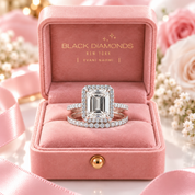 A silver-toned emerald-cut diamond ring with a halo and matching pavé band displayed in an open pink velvet ring box. The inside of the box is branded 'BLACK DIAMONDS NEW YORK | EVANI NAOMI'.