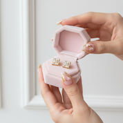 Hand holding a pink jewelry box with gold earrings inside against a white background