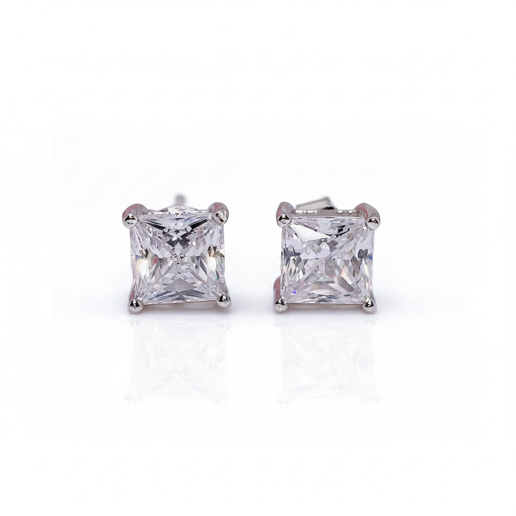 A pair of princess-cut diamond stud earrings in a silver four-prong setting, shown on a clean white background with a soft reflection below.