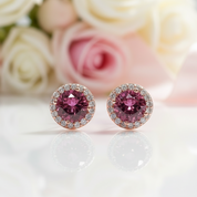 Pink gemstone earrings on a white surface with blurred flowers in the background