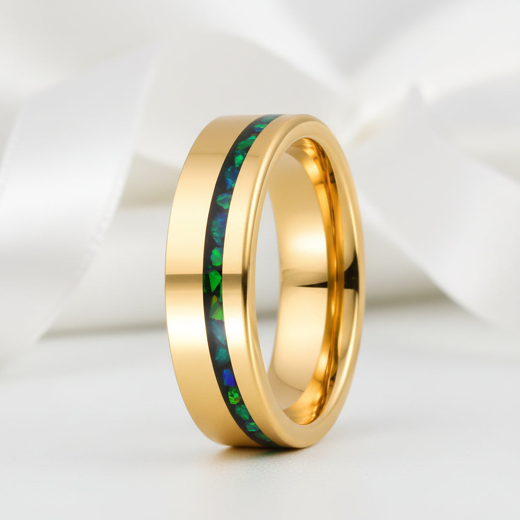 Gold ring with green and blue inlay on a white fabric background