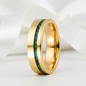 Gold ring with green and blue inlay on a white fabric background