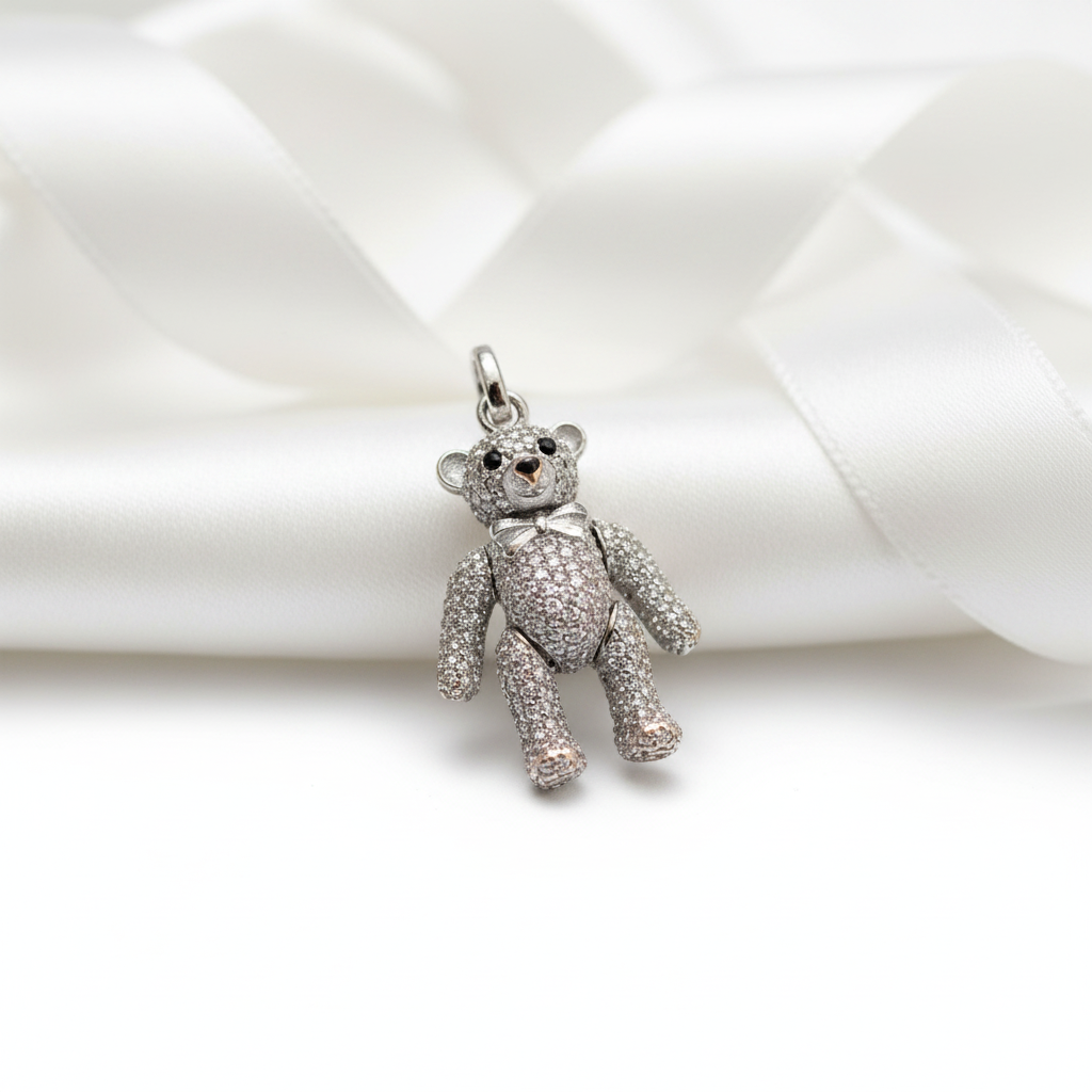 A silver teddy bear charm encrusted with clear rhinestones, resting on a white satin ribbon.