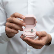 Person holding a pink jewelry box with a ring featuring a green gemstone.
