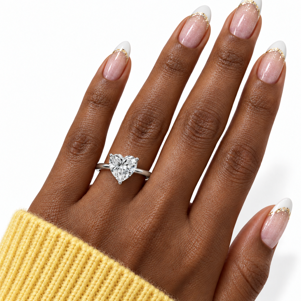 A heart-shaped diamond ring in a silver setting worn on a hand with a yellow knit sleeve visible, against a clean white background.
