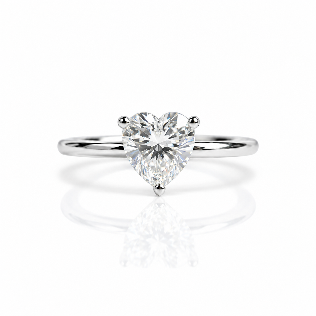 A heart-shaped diamond solitaire engagement ring on a polished silver band, set against a clean white background with a soft reflection below.