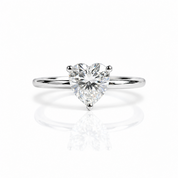 A heart-shaped diamond solitaire engagement ring on a polished silver band, set against a clean white background with a soft reflection below.