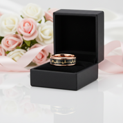 Gold ring with black engraving in a black box, flowers in the background