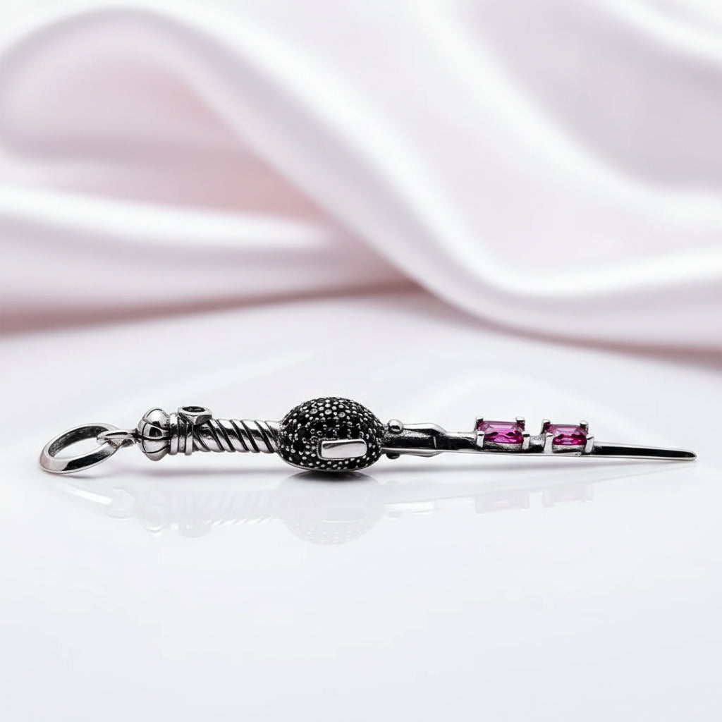 A silver-toned hair claw clip with a textured black ball accent and two small pink gemstones, displayed on a reflective white surface with draped white satin in the background.