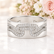 A silver-toned band ring featuring a wavy, shield-like design paved with small clear stones, shown on a clean white background with a soft reflection.