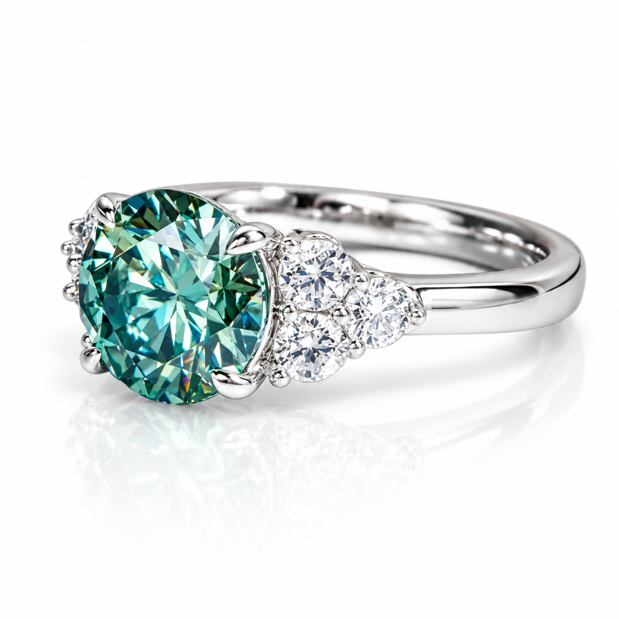 A silver ring featuring a large round-cut teal green center stone and a cluster of small clear stones on the band, shown on a white background with a soft reflection.