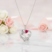A silver pendant necklace featuring a mother and child design with a small pink heart, displayed on a marble surface with soft pink and white roses in the background.