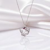 A silver pendant necklace featuring a heart-shaped silhouette of a mother and child, accented with a small red heart gemstone, displayed on a white satin background.
