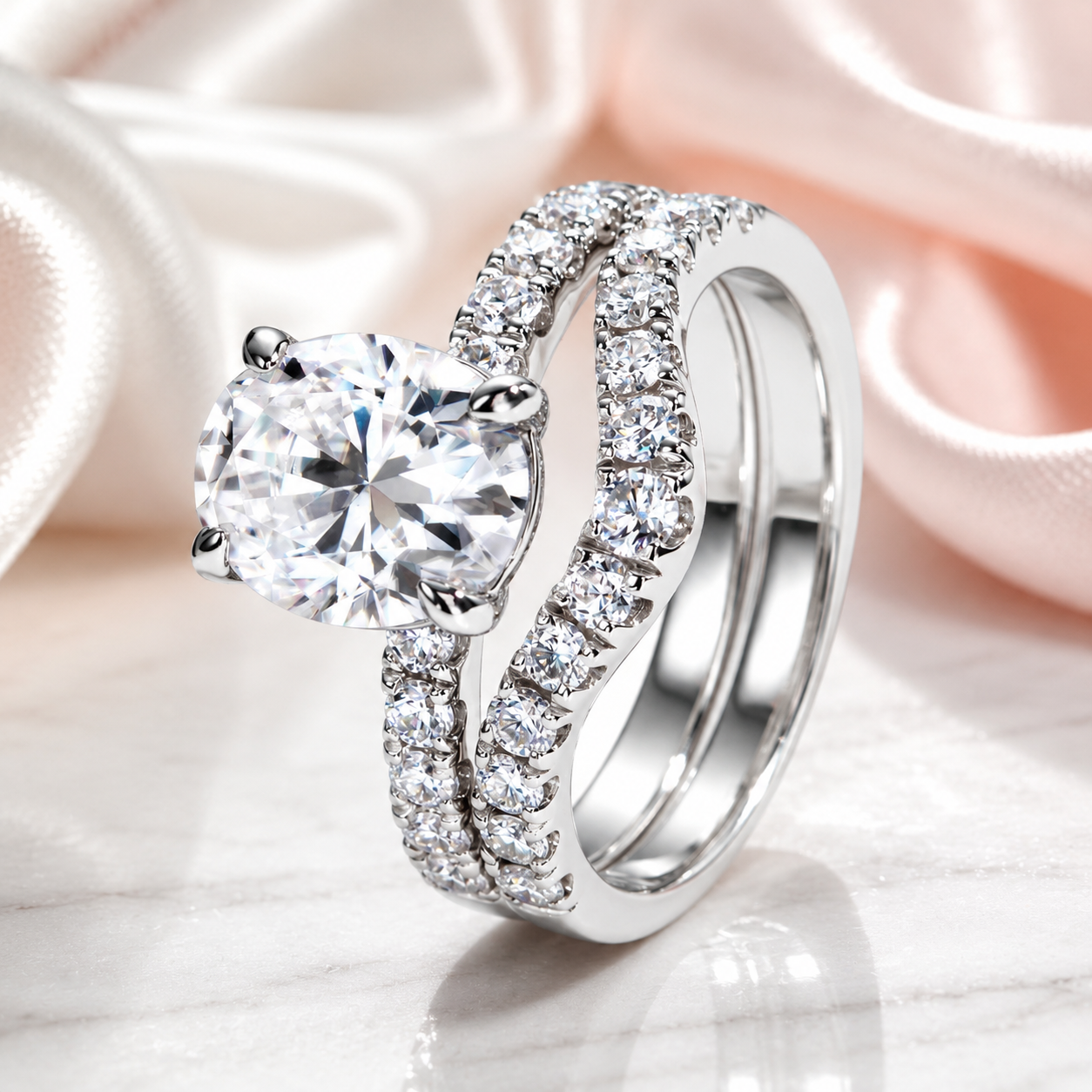 A silver-toned engagement ring with a large round brilliant-cut clear center stone and a matching pave-set band, displayed on a soft white and pink satin fabric background.