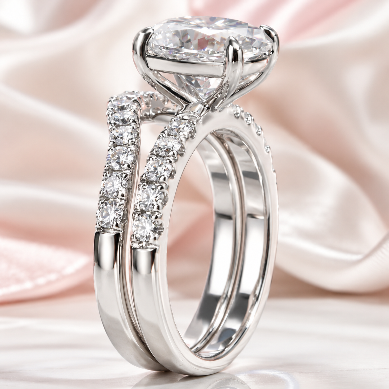 A silver-toned split-shank engagement ring with a large round brilliant-cut center stone and pavé-set accent stones, displayed on a soft pink satin fabric background.