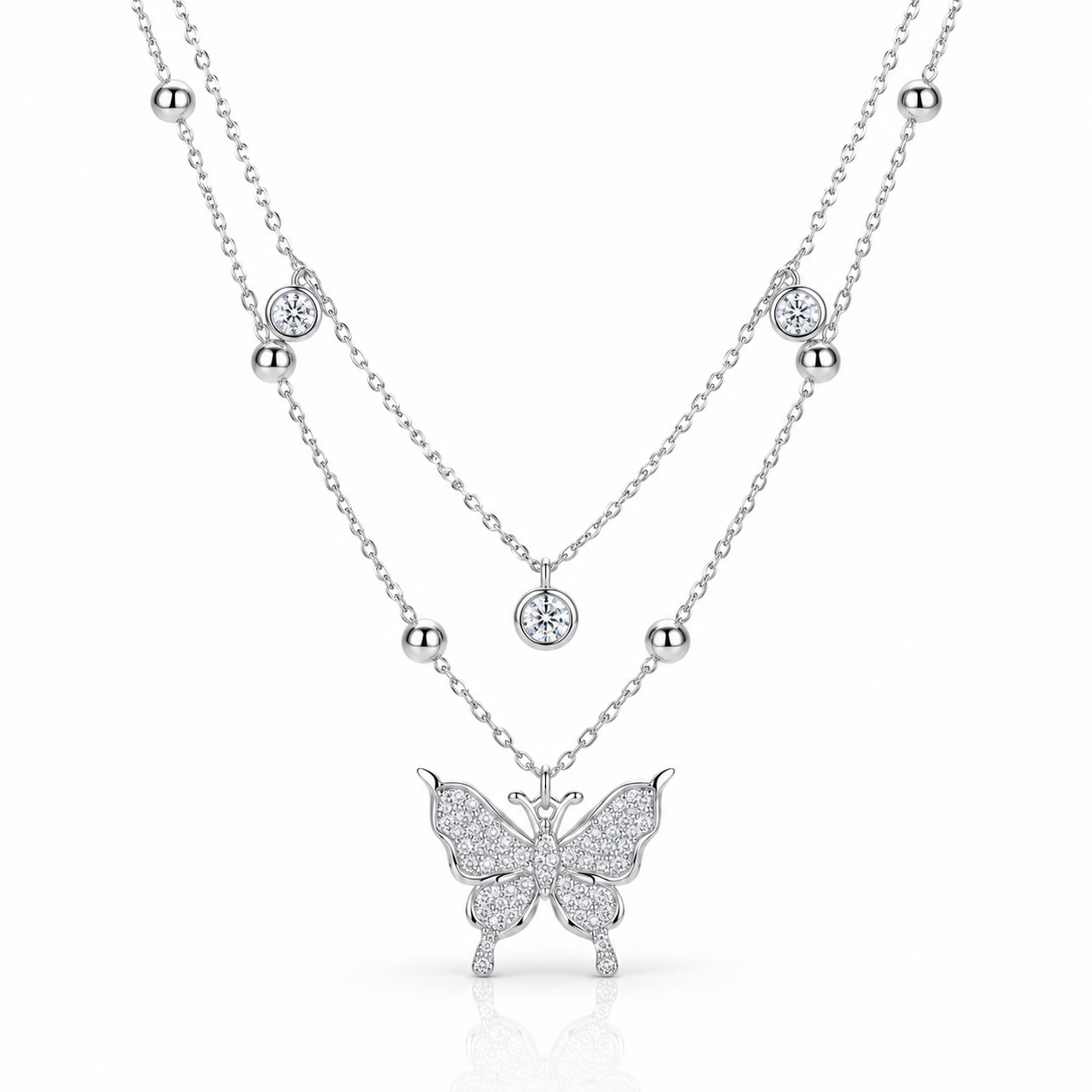 A silver-tone double-layer necklace featuring a delicate chain with small bead accents and round bezel-set clear stones, and a larger chain with a butterfly pendant paved with clear stones, shown on a white background.