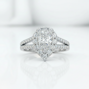 A pear-cut halo engagement ring in white metal with pavé-set diamonds, centered on a clean white reflective surface.