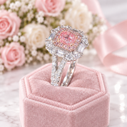 A pink cushioned ring box holding a silver-toned ring with a large pink center stone and clear baguette and round stones, set against soft pink roses and a pink ribbon.