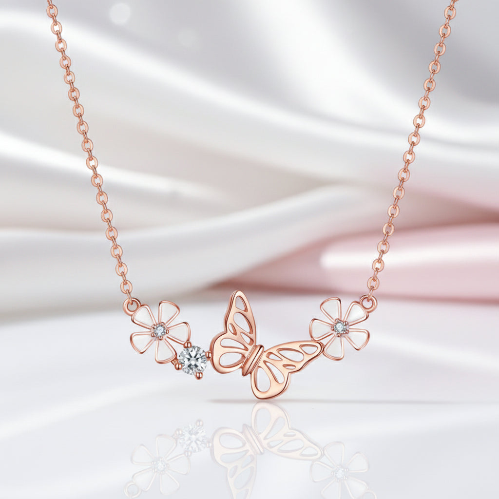 Rose gold necklace featuring a central butterfly pendant flanked by two flower motifs and a small clear crystal cluster, displayed on a soft white satin fabric background.