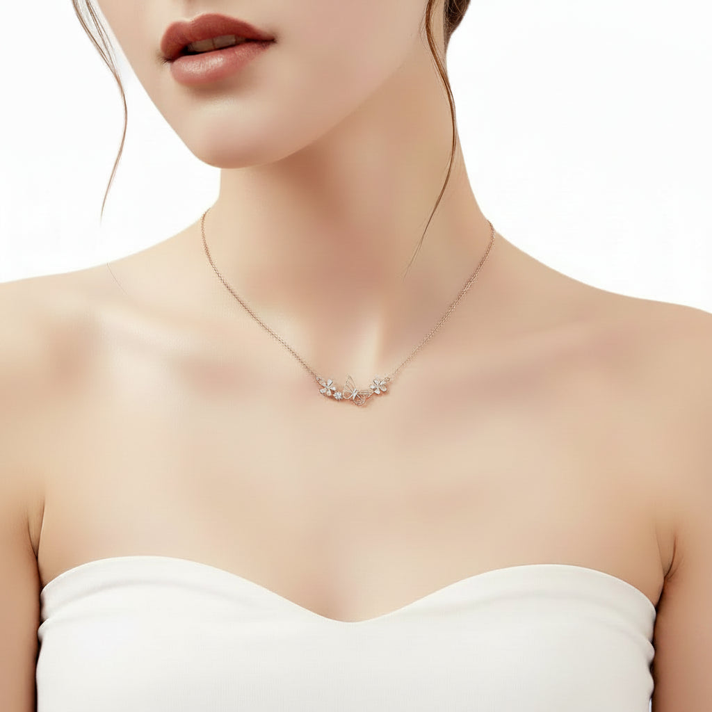 A close-up of a woman wearing a delicate rose gold necklace with a small floral cluster pendant, styled with a white strapless top against a clean white background.