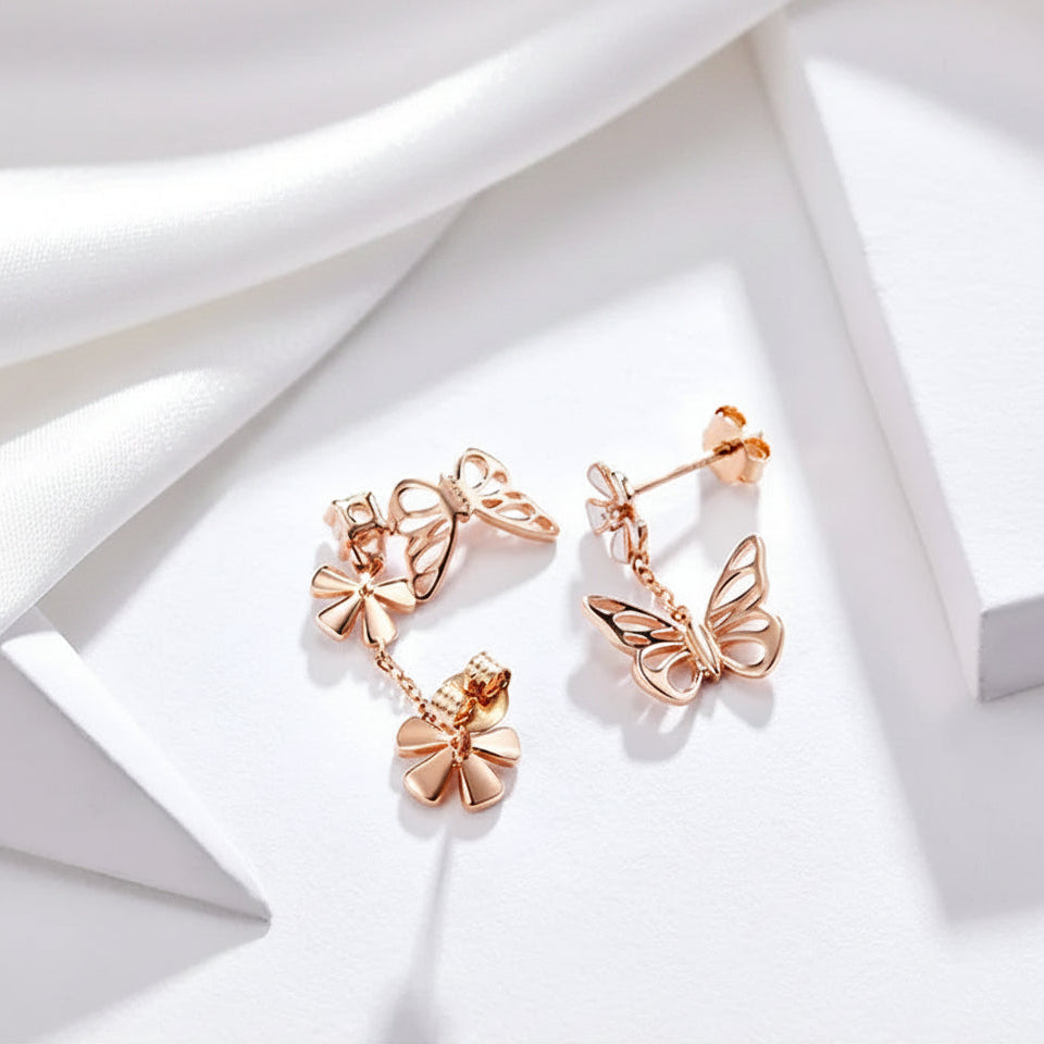 A pair of rose gold butterfly stud earrings with dangling bow charms, displayed on a clean white geometric surface with text at the top reading 'PRODUCT SHOWCASE AS UNIQUE AS YOU'.