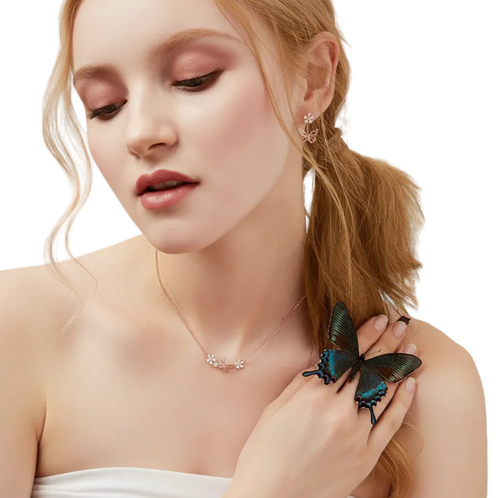 A close-up lifestyle shot of a woman with blonde hair tied back, wearing a delicate silver necklace and a silver ring adorned with a large, iridescent blue and green butterfly. She is wearing a white strapless top against a clean white background.