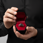 Person holding a black hexagonal jewelry box with a red interior containing a diamond ring.