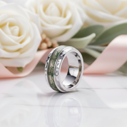 Silver ring with camouflage pattern on a reflective surface with white roses in the background
