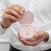 Person holding a pink jewelry box with a gold necklace featuring a heart-shaped pendant.