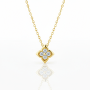 A gold necklace with a four-petal flower pendant set with clear round-cut gemstones, displayed on a clean white background with a soft reflection below.