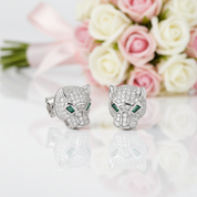 Silver panther head earrings with green gemstones in front of pink and white roses.