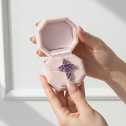 Hand holding a pink jewelry box with a purple cross pendant inside.