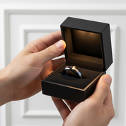 Person holding a black jewelry box with a ring inside against a white background