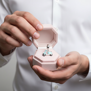 A close-up of a person's hands holding an open light pink jewelry box, displaying a miniature light blue scooter charm with silver and black details.