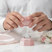 Person holding a pink jewelry box with a ring inside, surrounded by flowers on a light background