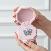 Butterfly necklace in a pink jewelry box held by a hand with white nail polish.