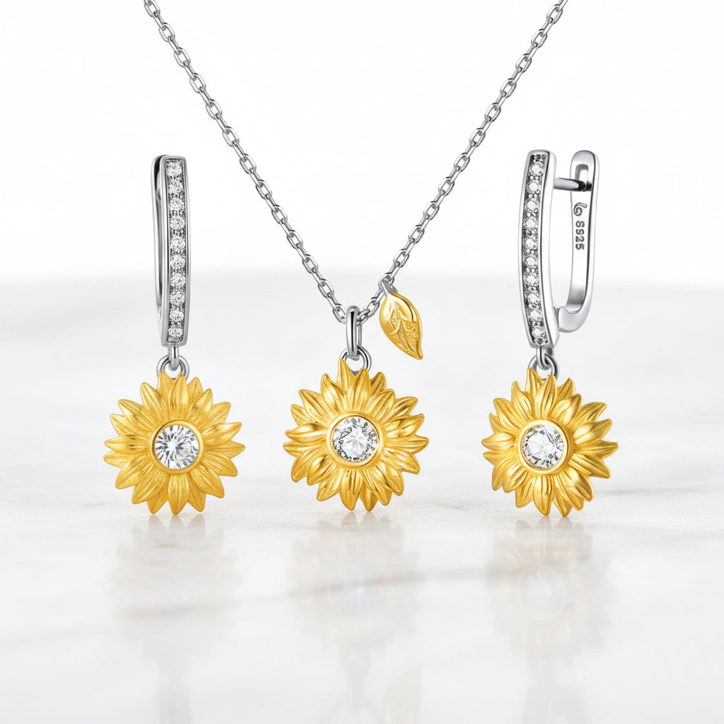 A jewelry set featuring a necklace and matching earrings with gold sunflower pendants and silver-toned hoops set with small clear stones, displayed on a white marble surface.