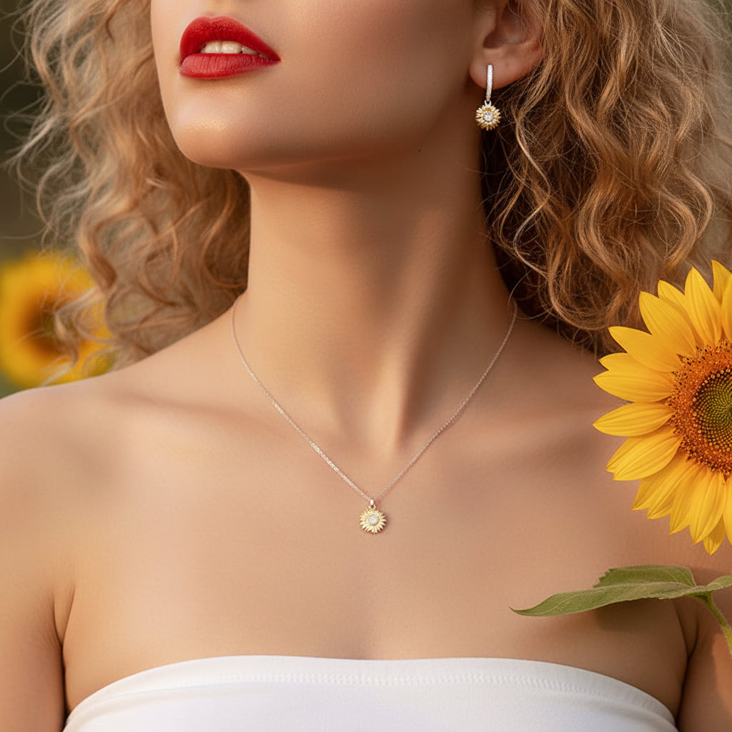 A close-up lifestyle shot of a woman wearing a delicate silver chain necklace with a small sunflower pendant and a matching drop earring. She has blonde curly hair, red lipstick, and is holding a yellow sunflower against a soft-focus background.