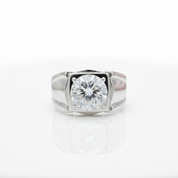 A silver-toned ring featuring a large round brilliant-cut gemstone in a square bezel setting, photographed on a clean white reflective surface.